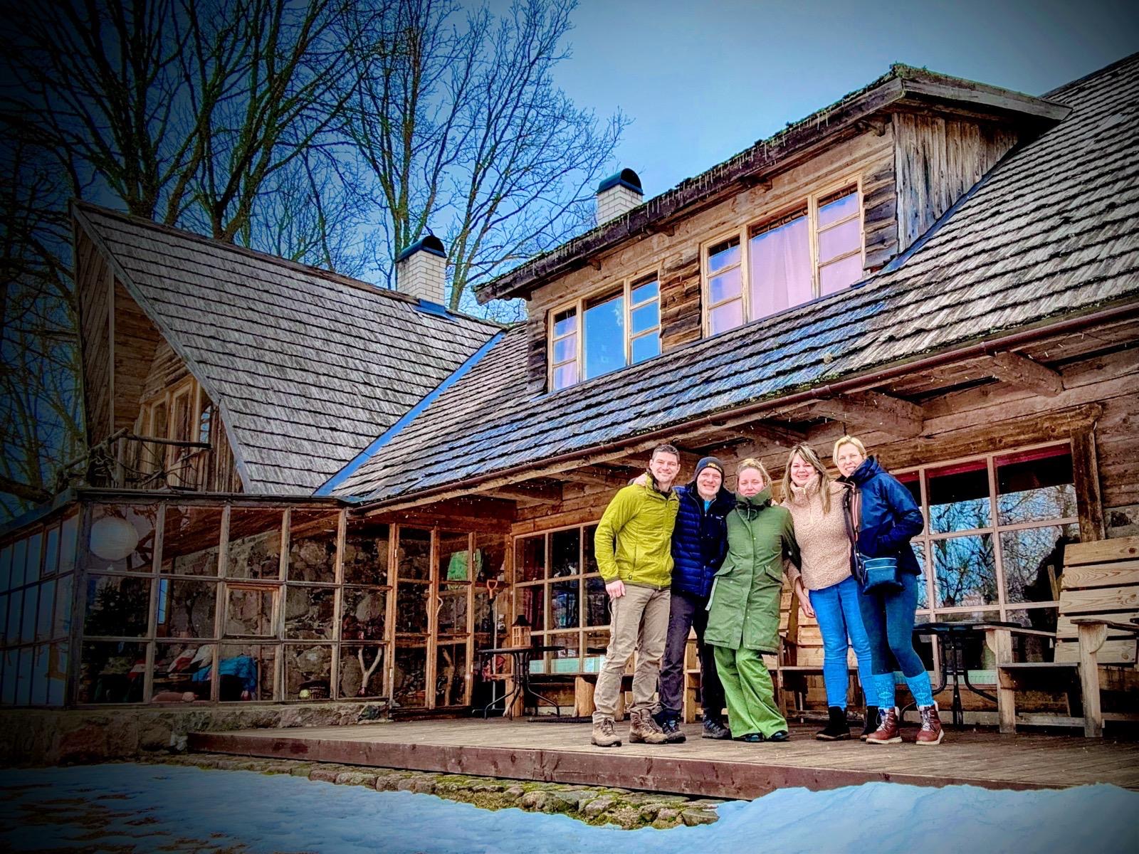 A small group standing together in front of an old Estonian farmhouse in winter